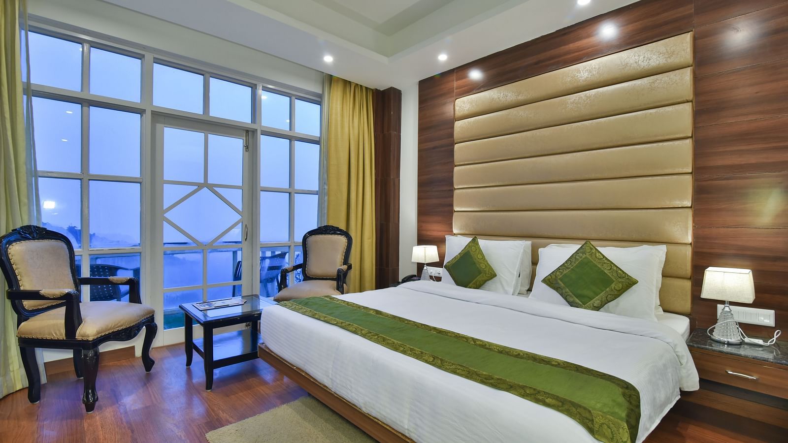 A large bed next to two chairs placed near a large window in the Premium Room at DLS Highland Resort and Spa, Mussoorie.